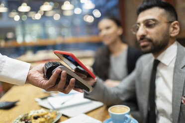 Geschäftsmann in einem Café, der mit seinem Smartphone kontaktlos bezahlt - CAIF21979