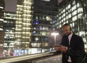 Businessman with headphones using digital tablet on urban pedestrian bridge at night - CAIF21982