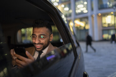 Businessman using smart phone in crowdsourced taxi at night - CAIF21993