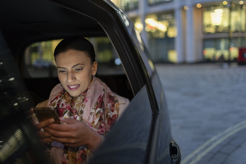 Geschäftsfrau, die nachts ihr Smartphone in einem Crowdsourced Taxi benutzt, lizenzfreies Stockfoto