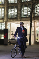 Geschäftsmann mit Fahrrad und Smartphone auf einem nächtlichen Bürgersteig - CAIF22013
