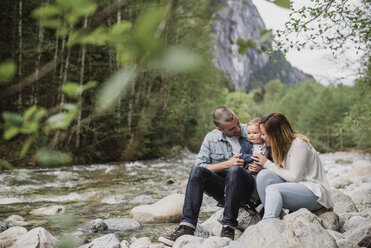 Eltern und kleiner Sohn sitzen auf Felsen am Bach - CAIF22035