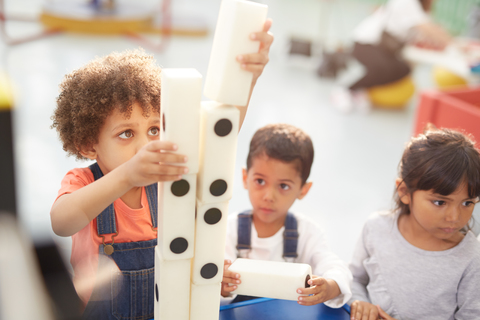 Neugierige Kinder stapeln große Dominosteine in der interaktiven Ausstellung im Wissenschaftszentrum, lizenzfreies Stockfoto