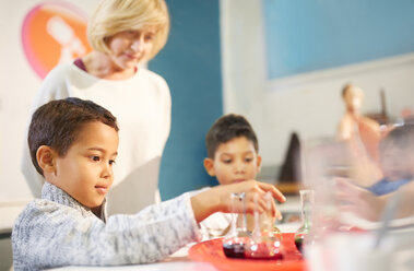 Teacher watching curious students playing with beakers at interactive exhibit in science center - CAIF22083