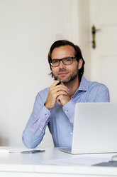 Portrait of confident businessman sitting at desk with laptop - HHLMF00376