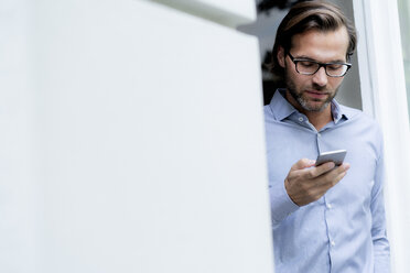 Mann steht im Türrahmen und benutzt ein Mobiltelefon - HHLMF00381