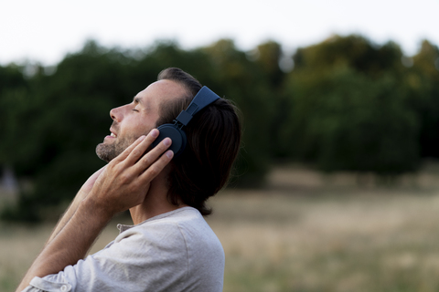 Lächelnder Mann, der mit Kopfhörern in der Natur Musik hört, lizenzfreies Stockfoto