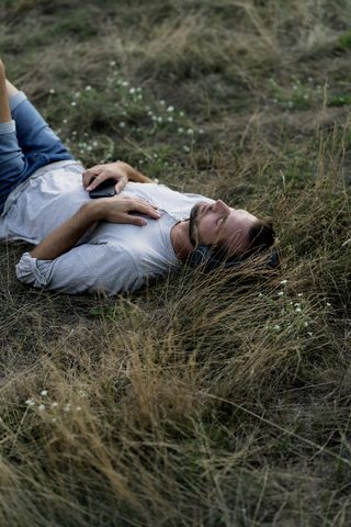 Entspannter Mann, der auf einem Feld liegt und mit Kopfhörern Musik hört, lizenzfreies Stockfoto