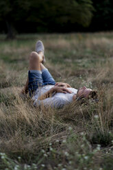 Entspannter Mann, der auf einem Feld liegt und mit Kopfhörern Musik hört - HHLMF00386