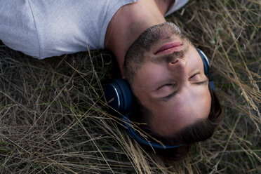 Relaxed man lying in field listening to music with headphones - HHLMF00387