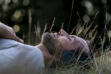 Entspannter Mann, der auf einem Feld liegt und mit Kopfhörern Musik hört - HHLMF00388