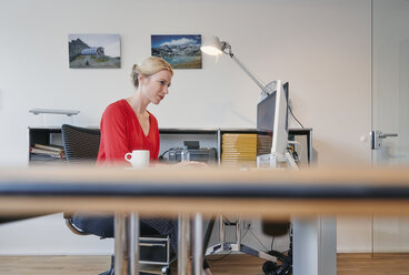 Junge Frau arbeitet am Computer am Schreibtisch im Büro - RHF02095