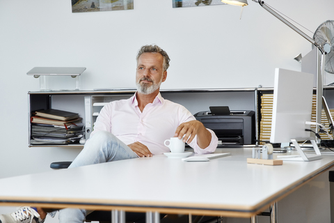 Businessman sitting at desk in office thinking stock photo