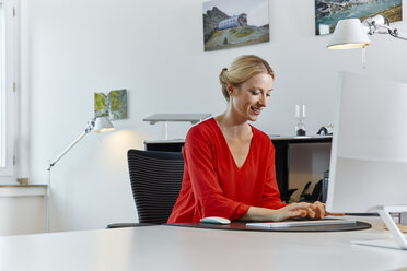 Lächelnde junge Frau arbeitet am Computer am Schreibtisch im Büro - RHF02111