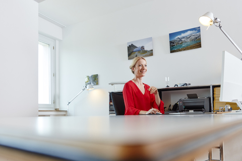 Lächelnde junge Frau arbeitet am Computer am Schreibtisch im Büro, lizenzfreies Stockfoto