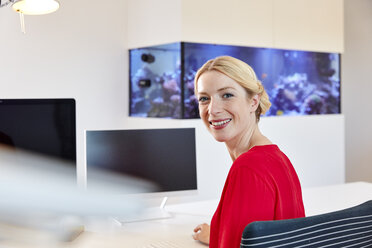 Porträt einer lächelnden jungen Frau, die am Schreibtisch im Büro sitzt - RHF02118