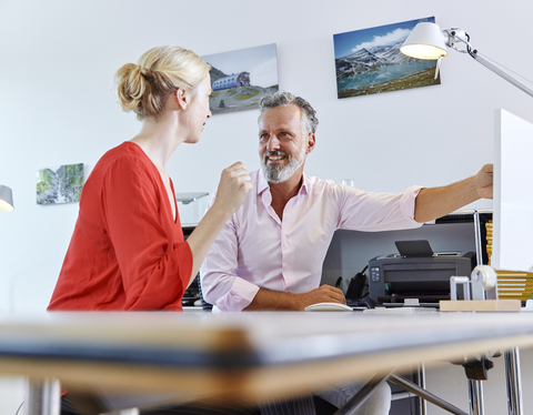 Zwei Kollegen unterhalten sich am Schreibtisch im Büro, lizenzfreies Stockfoto