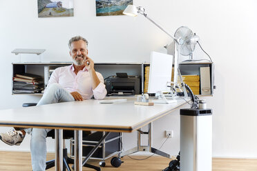 Porträt eines lächelnden Geschäftsmannes, der am Schreibtisch im Büro sitzt - RHF02130