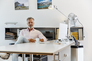 Portrait of confident businessman sitting at desk in office - RHF02131