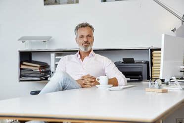 Portrait of confident businessman sitting at desk in office - RHF02132