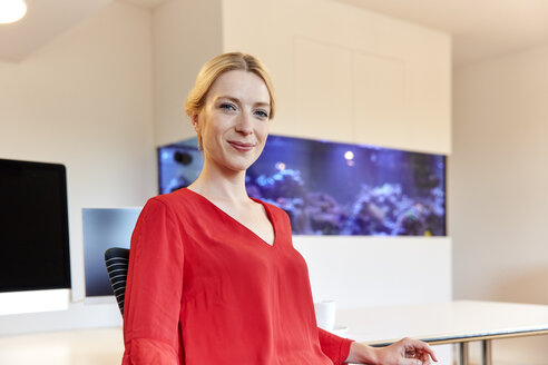 Portrait of smiling young woman sitting at desk in office - RHF02139