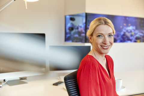 Porträt einer lächelnden jungen Frau, die am Schreibtisch im Büro sitzt, lizenzfreies Stockfoto