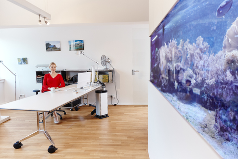 Junge Frau sitzt am Schreibtisch im Büro mit einem Aquarium, lizenzfreies Stockfoto