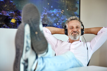 Relaxed mature man listening to music with headphones in front of aquarium - RHF02161