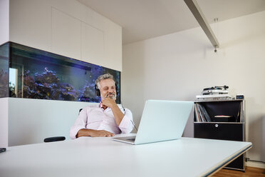 Geschäftsmann mit Kopfhörern und Laptop am Schreibtisch vor einem Aquarium - RHF02163