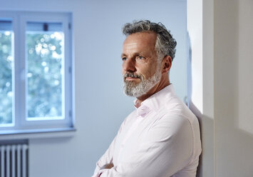 Portrait of mature man leaning against doorframe in office thinking - RHF02189