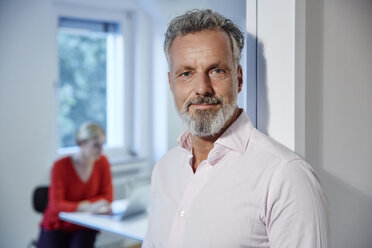 Portrait of mature man ln office with colleague in background - RHF02190