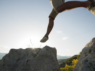 Mann springt auf Felsen über dem Meer - AURF04694