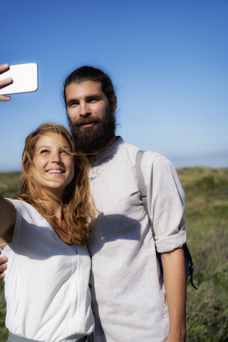 Junges Paar macht Smartphone-Selfies am Strand, lizenzfreies Stockfoto
