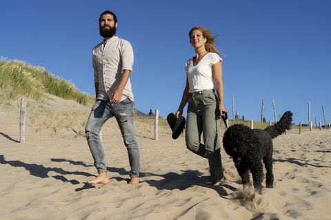 Junges Paar geht mit seinem Hund am Strand spazieren, lizenzfreies Stockfoto