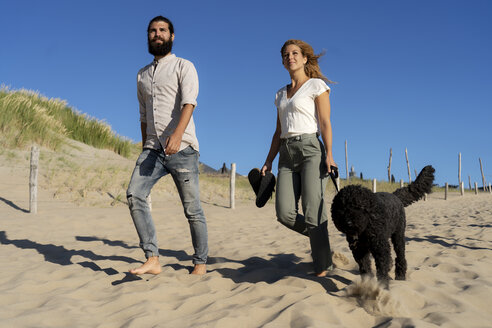 Junges Paar geht mit seinem Hund am Strand spazieren - HHLMF00431