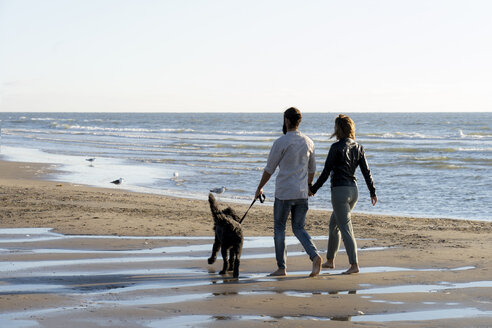 Junges Paar geht mit seinem Hund am Strand spazieren - HHLMF00446