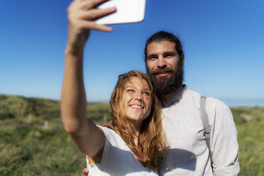 Young couple taking smartphone selfies on the beach - HHLMF00452