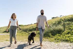 Junges Paar geht mit seinem Hund am Strand spazieren - HHLMF00454