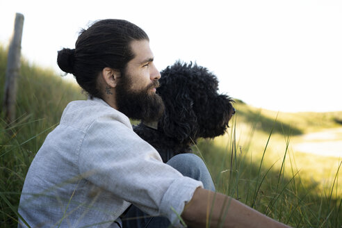 Junger Mann sitzt mit seinem Hund in den Dünen - HHLMF00456