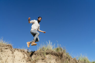 Young man jumping from a sand dune - HHLMF00464