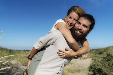 Young man carrying his girlfriend piggyback in the dunes - HHLMF00469