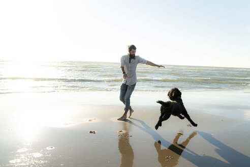 Young man running and playing with his dog on the beach - HHLMF00473