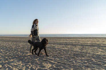 Junge Frau, die mit ihrem Hund am Strand spazieren geht - HHLMF00486