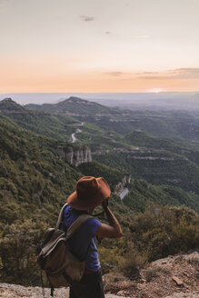 Spanien, Barcelona, Montserrat, Mann mit Rucksack beim Fotografieren der Aussicht bei Sonnenuntergang - AFVF01550