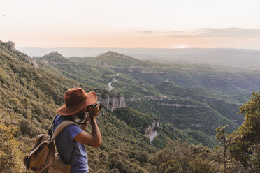 Spanien, Barcelona, Montserrat, Mann mit Rucksack beim Fotografieren der Aussicht bei Sonnenuntergang - AFVF01551