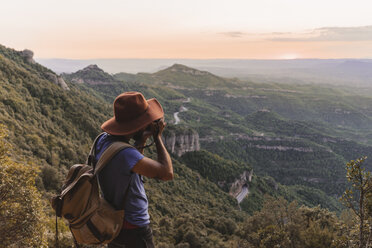 Spain, Barcelona, Montserrat, man with backpack taking photo of view at sunset - AFVF01552