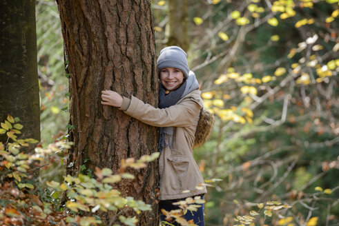 Porträt eines lächelnden Teenagers, der sich in einem herbstlichen Wald an einen Baumstamm schmiegt - LBF02044