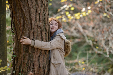 Portrait of smiling teenage girl hugging tree trunk in autumnal forest - LBF02045
