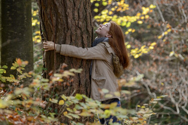 Happy teenage girl hugging tree trunk in autumnal forest - LBF02048