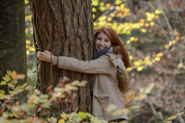 Porträt eines glücklichen Teenagers, der sich in einem herbstlichen Wald an einen Baumstamm schmiegt - LBF02049